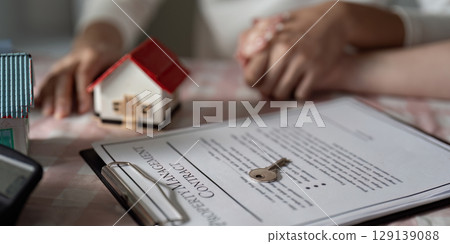 Professional Real Estate Agent with House Model and Contract Document in Office Setting Professional Real Estate Agent with House Model and Contract Document in Office Setting 129139088