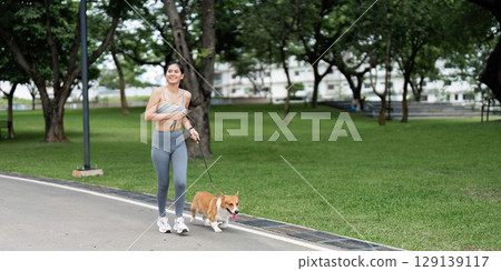 Joyful Woman Running with Corgi in Urban Park 129139117