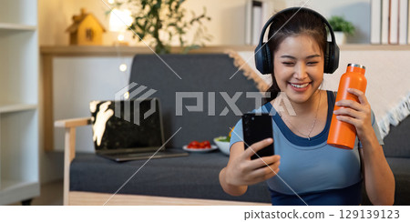 Joyful Moments. Young woman enjoying music and taking a selfie at home, celebrating wellness and connection. 129139123