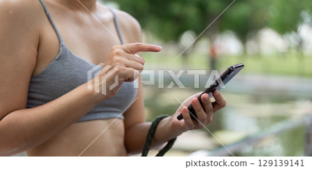 Focused on Fitness. Woman Using Smartphone in Park 129139141