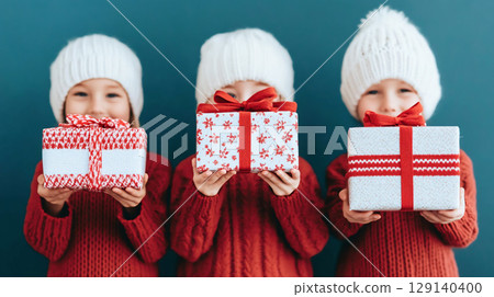 joyful children holding gift during Christmas celebrations with family gathering together. festive holiday seasonal Christmas New Year atmosphere is enhanced by decorated tree and smiling faces 129140400