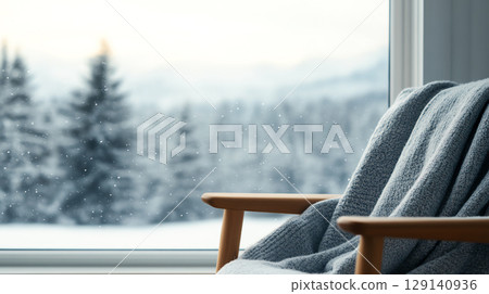Cozy chair with blanket by window, snow falling outside, winter scene. Perfect for relaxation and warmth during cold days 129140936