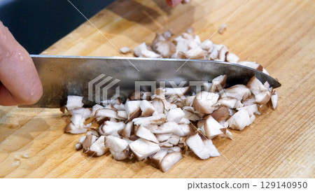 Shiitake mushrooms being chopped finely with a knife on a wooden cutting board 129140950