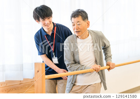 老年男子利用扶手進行步行訓練，由職能治療師和男性物理治療師陪同 129141580