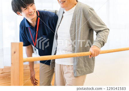 老年男子利用扶手進行步行訓練，由職能治療師和男性物理治療師陪同 129141583