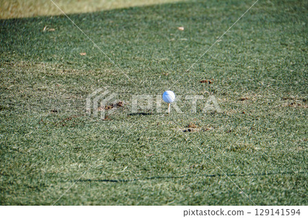 Green grass and a white golf ball on a tee 129141594