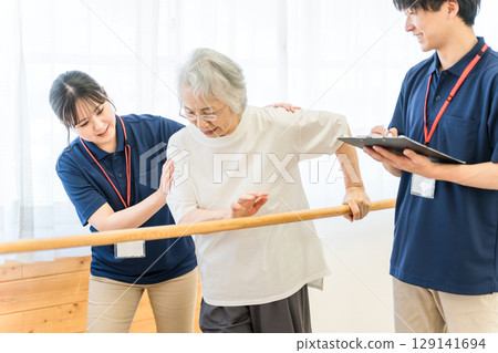 老年婦女使用扶手進行步行訓練，男女職能治療師和物理治療師工作人員協助她 129141694