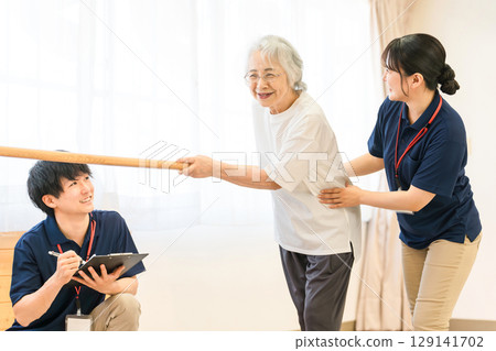 Senior woman using handrail for walking training Male and female physiotherapist staff treating Senior woman using handrail for walking training Male and female physiotherapist staff treating 129141702