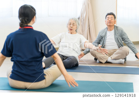 Seniors doing stretching and yoga at the gym, nursing home, welfare center, elderly men and women, caregivers, trainers Seniors doing stretching and yoga at the gym, nursing home, welfare center, elderly men and women, caregivers, trainers 129141918