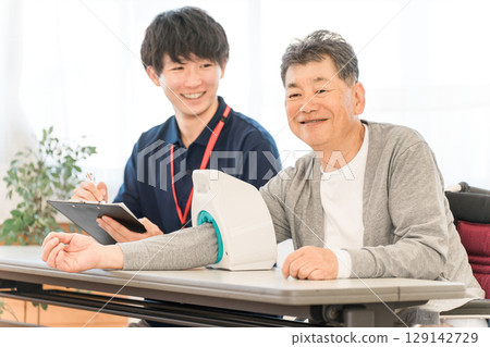 一位老人用血壓計測量血壓,一位護士做筆記,一位男性護理人員 一位老人用血壓計測量血壓,一位護士做筆記,一位男性護理人員 129142729