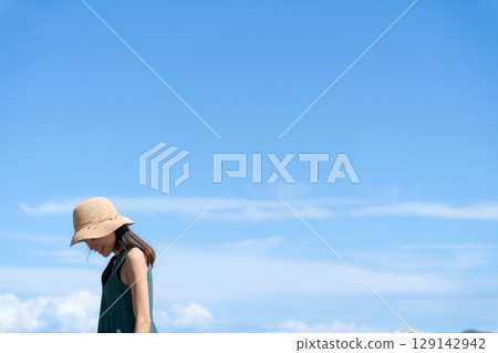 Young woman wearing a straw hat against the blue sky 129142942