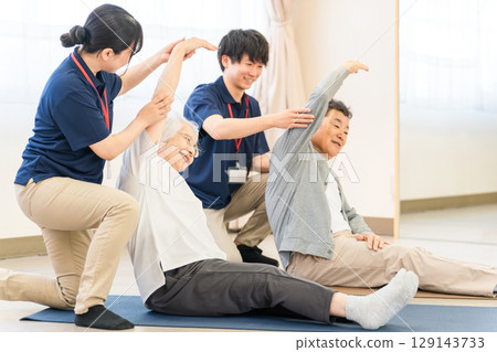 Rehabilitation at a care facility, welfare center, seniors stretching, elderly men and women with occupational therapists, caregivers, trainers Rehabilitation at a care facility, welfare center, seniors stretching, elderly men and women with occupational therapists, caregivers, trainers 129143733