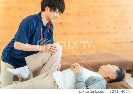 一位老年男子在復健期間接受按摩和伸展運動,以及包括物理治療師和職業治療師在內的男性工作人員 一位老年男子在復健期間接受按摩和伸展運動,以及包括物理治療師和職業治療師在內的男性工作人員 129144034