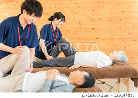 一位老年男子在復健期間接受按摩和伸展運動,以及包括物理治療師和職業治療師在內的男性工作人員 一位老年男子在復健期間接受按摩和伸展運動,以及包括物理治療師和職業治療師在內的男性工作人員 129144035