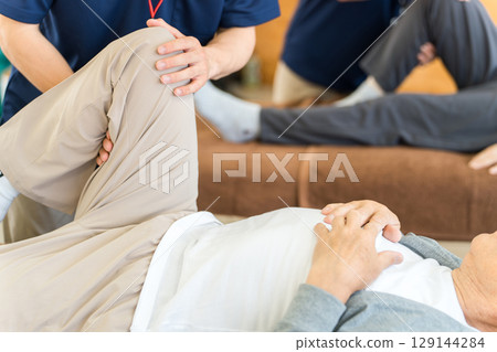 Orthopedic surgery, senior man receiving treatment from a physiotherapist on a treatment bed in a hospital Orthopedic surgery, senior man receiving treatment from a physiotherapist on a treatment bed in a hospital 129144284