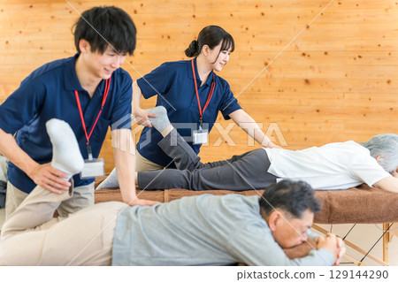 一位老年男子在復健期間接受按摩和伸展運動，以及包括物理治療師和職業治療師在內的男性工作人員 129144290