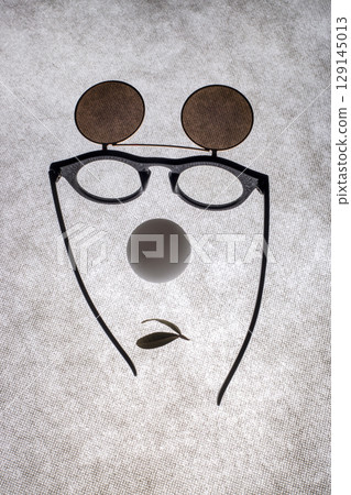 Sunglasses with double glass, a white ball and a leaf in the shape of a face on a gray background 129145013