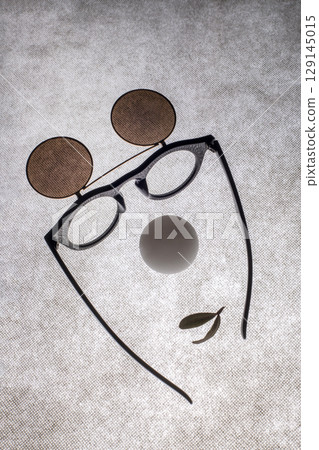 Sunglasses with double glass, a white ball and a leaf in the shape of a face on a gray background 129145015
