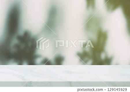 White Marble Tabletop in the Foreground with a Blurred Background of Green foliage and Light Leak. White Marble Tabletop in the Foreground with a Blurred Background of Green foliage and Light Leak. 129145929