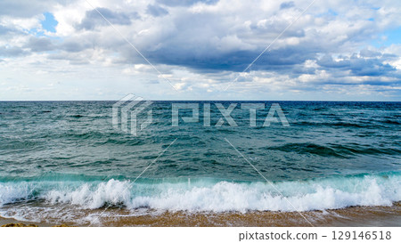 A coastal landscape with a vast blue sea and white waves crashing against a cloudy sky A coastal landscape with a vast blue sea and white waves crashing against a cloudy sky 129146518