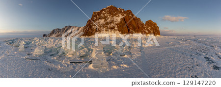 Beautiful winter landscape of frozen Lake Baikal at sunrise - A granite rock with steep slopes rises above a frozen lake - Baikal lake, Siberia. Winter ice covers providing a stunning backdrop for Beautiful winter landscape of frozen Lake Baikal at sunrise - A granite rock with steep slopes rises above a frozen lake - Baikal lake, Siberia. Winter ice covers providing a stunning backdrop for 129147220