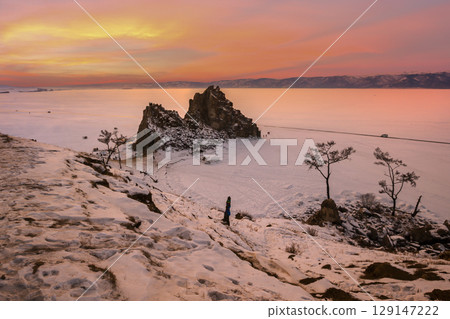 Baikal Lake in December. Magnificent sunset landscape of Olkhon Island in snowy weather. View of the natural landmark - Shamanka Rock and the Wish Tree. 129147222