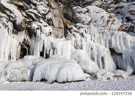 Baikal Lake in the winter cold day. Beautiful icy rocks with big ice crust.long icicles on the icy coastal cliffs of Olkhon Island Baikal Lake in the winter cold day. Beautiful icy rocks with big ice crust.long icicles on the icy coastal cliffs of Olkhon Island 129147256