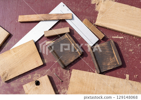 Woodworking elements arranged on a reddish surface two dark grooved blocks, two screws, a carpenter square, and light wood pieces Woodworking elements arranged on a reddish surface two dark grooved blocks, two screws, a carpenter square, and light wood pieces 129148068