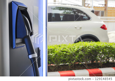 Electric car charging on parking lot with electric car charging station on city street. Close up of power supply plugged into an electric car being charged. 129148545