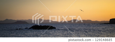 A small island in the beautiful ocean with small waves in the evening at sunset. A small island in the beautiful ocean with small waves in the evening at sunset. 129148685