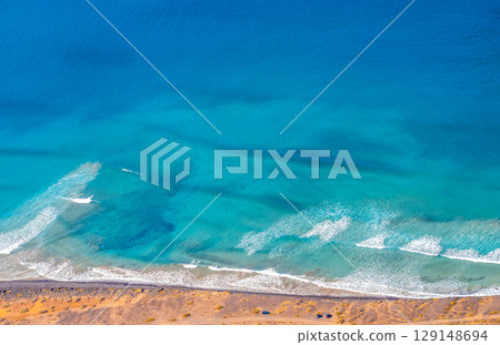 Blue ocean with waves and a sandy beach, top view. Blue ocean with waves and a sandy beach, top view. 129148694