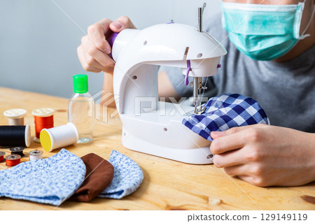 Woman sewing cloth cotton face mask to protect against the corona virus at home. Homemade handicraft protective mask against covid 19 virus. Reusable face mask. 129149119