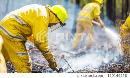 Firefighters combat forest wildfire in protective gear, creating dense smoke 129149258