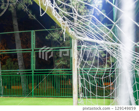football field in the evening.  Artificial lawn. Available infrastructure. Empty sports ground. Football game concept. Entertainment in the park. Empty. Football goal net. Under the lanterns 129149859