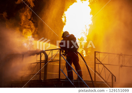 Firefighter training, fireman using water and extinguisher to fighting with fire flame in an emergency situation., under danger situation all firemen wearing fire fighter suit for safety. 129151099