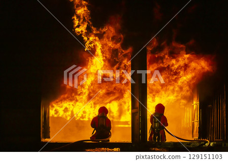 Firefighter training, fireman using water and extinguisher to fighting with fire flame in an emergency situation., under danger situation all firemen wearing fire fighter suit for safety. 129151103