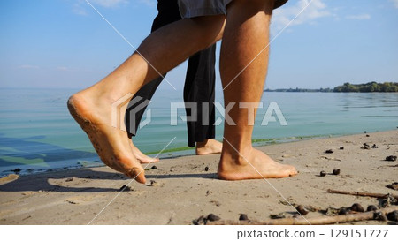 Bare feet of couple stepping together along sand beach at coastline. Male and female legs of pair walking near seaside. Happy lovers going along sandy shore. Concept of summer vacation or holiday Bare feet of couple stepping together along sand beach at coastline. Male and female legs of pair walking near seaside. Happy lovers going along sandy shore. Concept of summer vacation or holiday 129151727