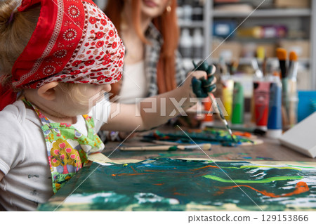 A Creative Child Enthusiastically Painting with Their Mother in a Vibrant Art Studio 129153866