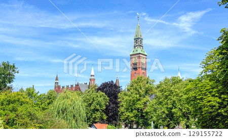 The tower of the Copenhagen City Hall against a blue sky and green trees 129155722