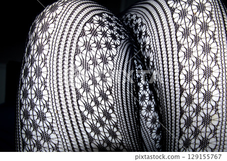 Close up of black lace fishnet tights on skin legs curves abstract background 129155767