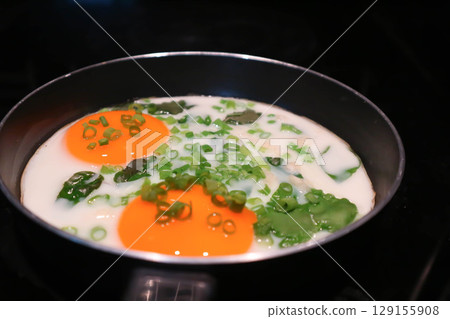 fried egg or sunny side up egg with vegetable topping in a pan 129155908