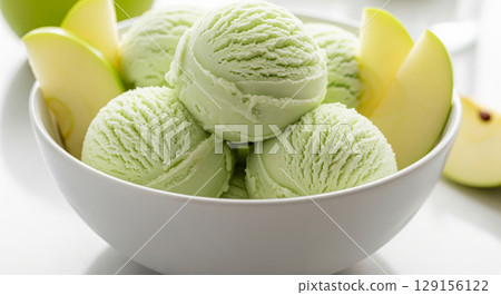 Close-up of a white bowl filled with three scoops of apple ice cream, garnished with a apple slices. 129156122