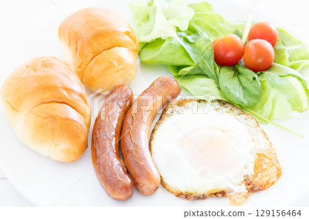 A delicious breakfast on a plate of buttered rolls, sausages, fried eggs and salad 129156464