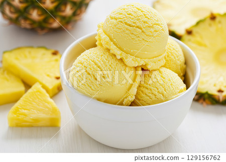 Close-up of a white bowl filled with three scoops of pineapple ice cream, garnished with a pineapple slices.  129156762