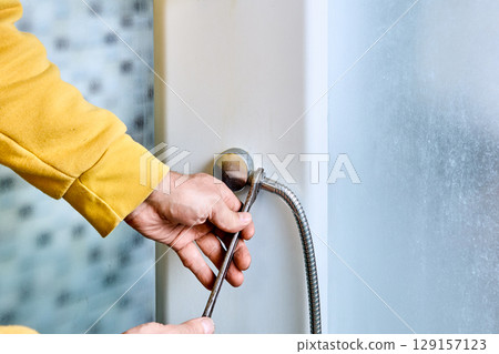 Flexible shower hose connection process shows installer tightening hose onto shower mixer outlet using open-end wrench with clear detail of threading at attachment point. Flexible shower hose connection process shows installer tightening hose onto shower mixer outlet using open-end wrench with clear detail of threading at attachment point. 129157123