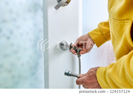 Flexible shower hose is being mounted onto shower valve by installer with double ended wrench inside shower enclosure during installation process 129157124