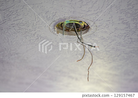 Exposed electrical wires hanging from a ceiling fixture in a residential setting during daylight hours Exposed electrical wires hanging from a ceiling fixture in a residential setting during daylight hours 129157467