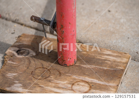 Support post anchored to wooden base on pavement for construction project in urban area during daylight hours 129157531