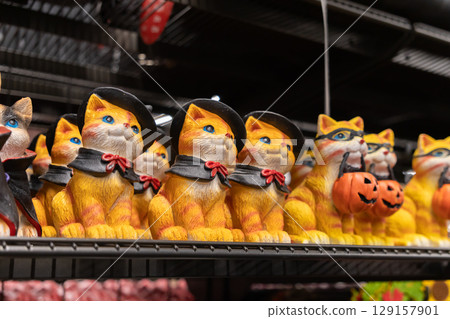 Row of charming Halloween cat figurines dressed in festive costumes, including Puss in Boots style and masked trick-or-treaters, perfect for holiday decor or retail displays 129157901