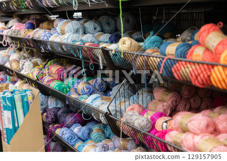 Rows of vibrant colorful yarn skeins stacked neatly on shelves in a craft store, showcasing a wide selection for creative hobby projects and knitting 129157905